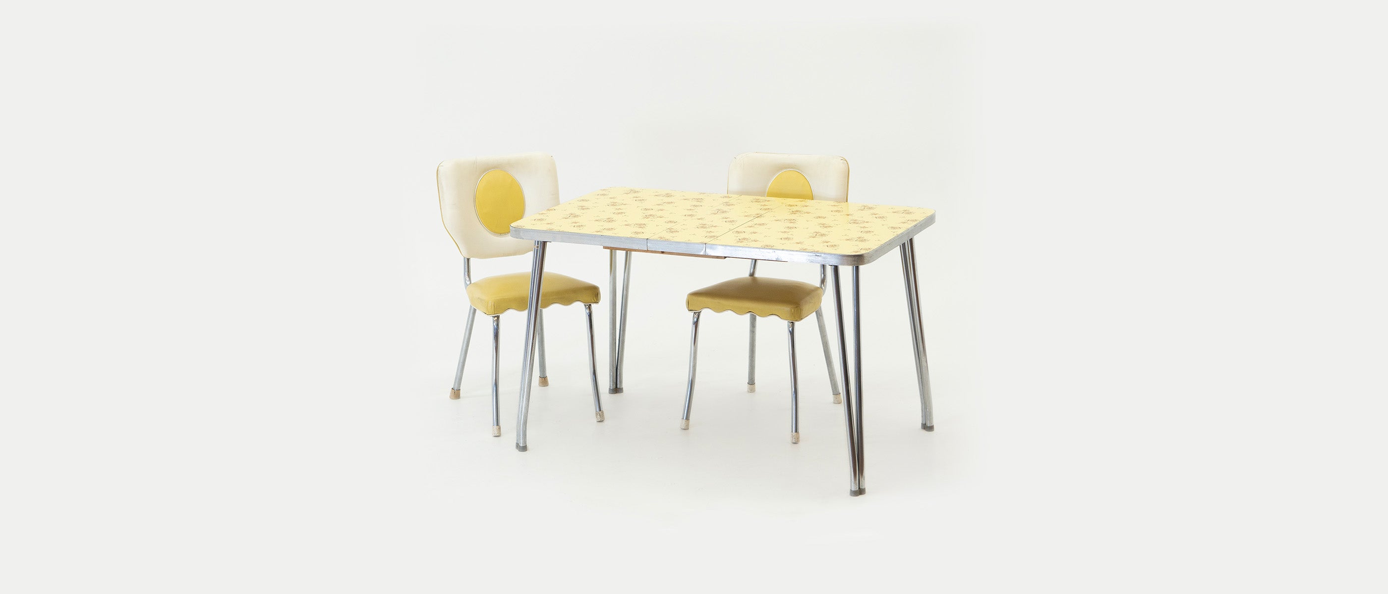 Yellow and chrome dinette set from the 1950s on a white background. Two chairs and one table.