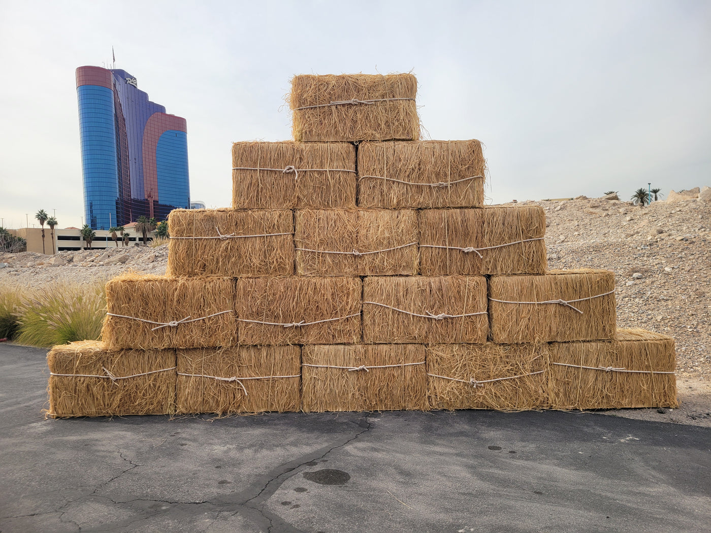 Stack of faux hay bales in a desert-like setting with modern buildings in the background