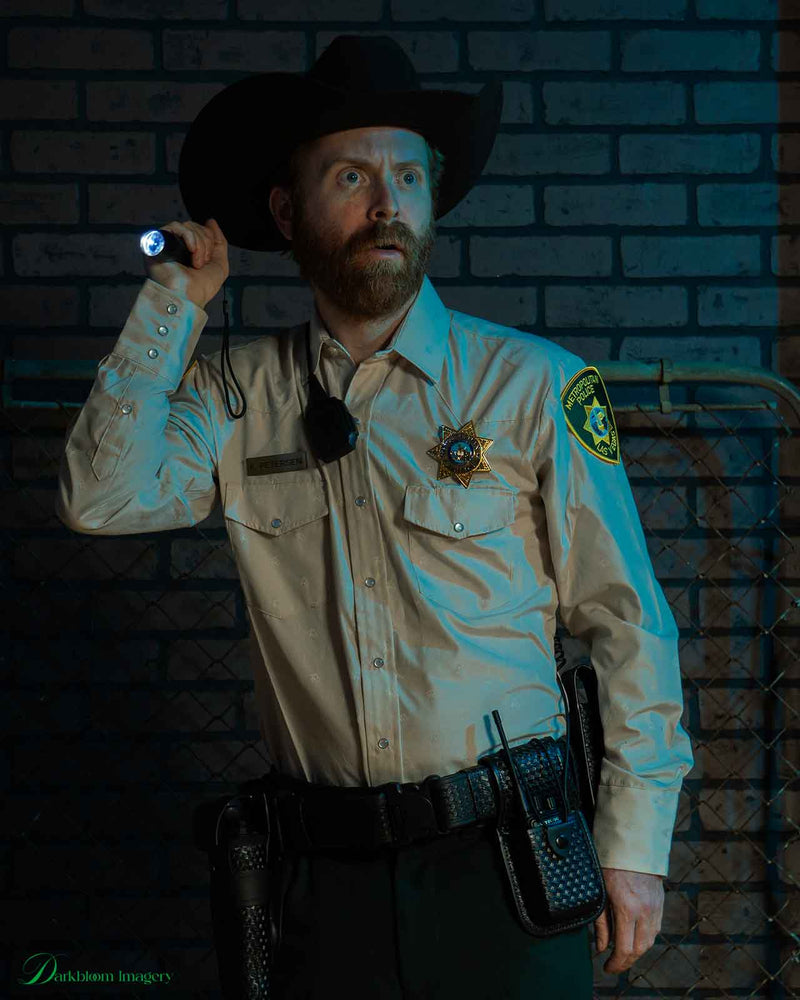 Person in a sheriff costume holding a flashlight against a brick wall.
